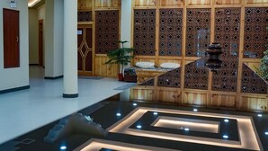 A modern lobby with a central water feature, wooden paneling, and recessed lighting. - Hotel Karma Residency (Leh)