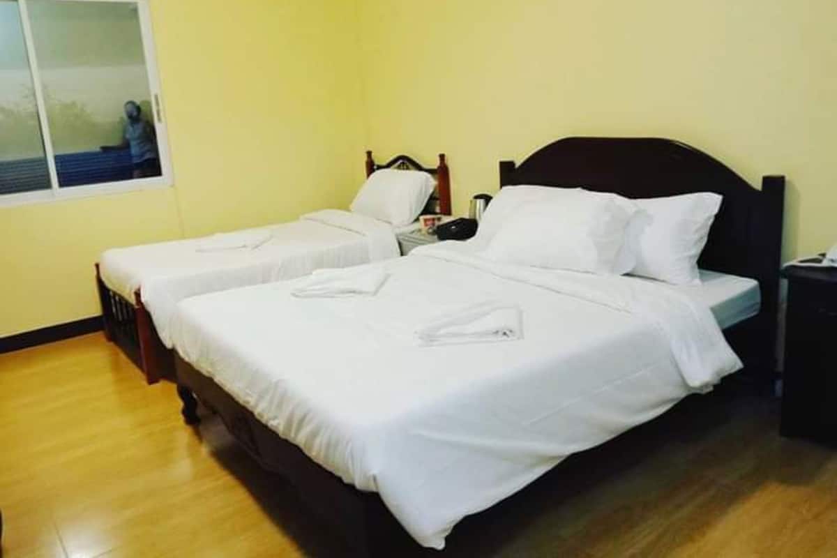 A room with two single beds, wooden headboards, white bedding, a small bedside table with a lamp, and a window with a view of a person outside.