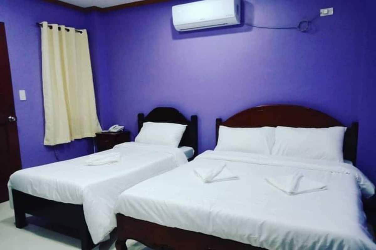 A room with two single beds, a nightstand with a phone, and an air conditioning unit on the wall.