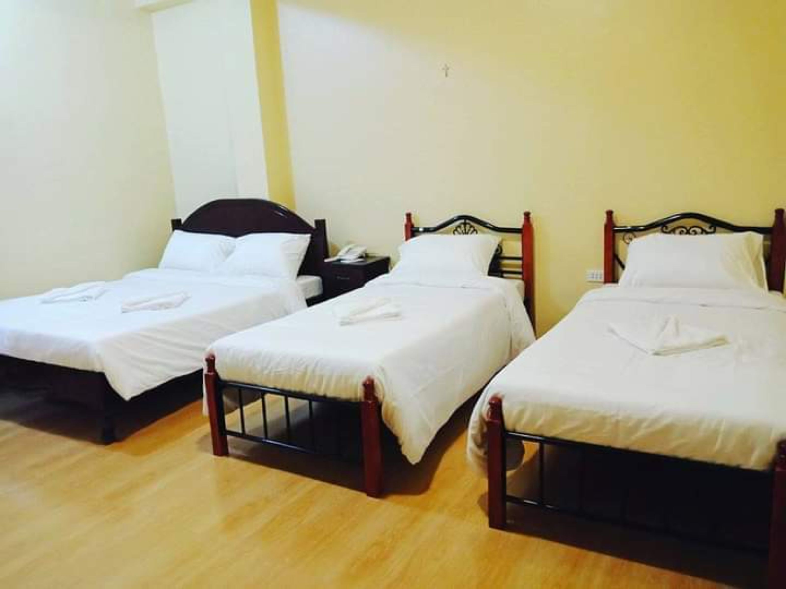A room with three single beds, each with a wooden frame and white bedding.