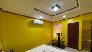 A hotel room with a bed, a small table, an air conditioning unit, a door, and a curtain. - Casa Venicia Caticlan (Boracay Island)