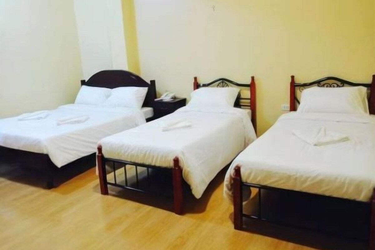 Two single beds with wooden frames and white bedding in a room with wooden flooring and plain walls.