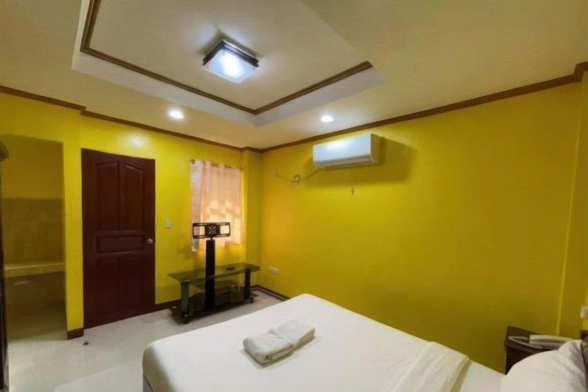 A hotel room with a bed, a desk, a mirror, and a window with curtains.
