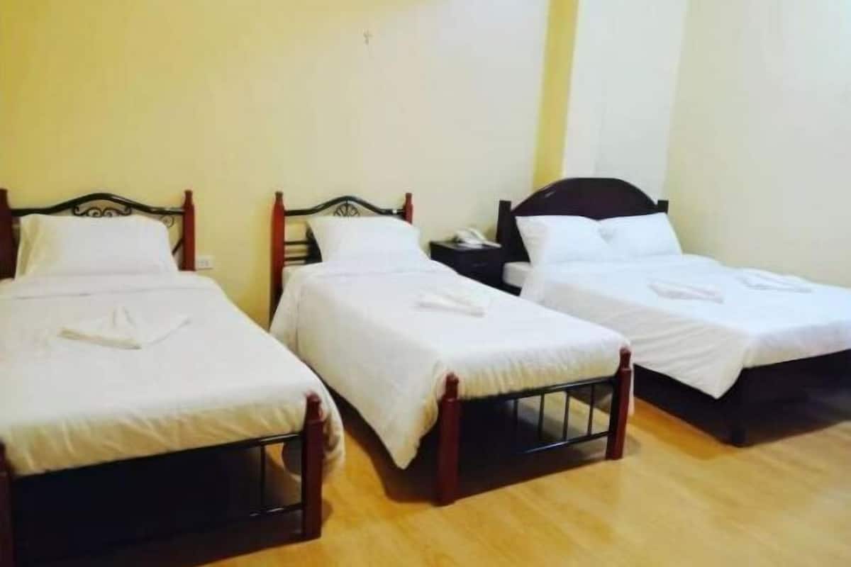 Three single beds with wooden frames and white bedding in a room with wooden flooring and plain walls.