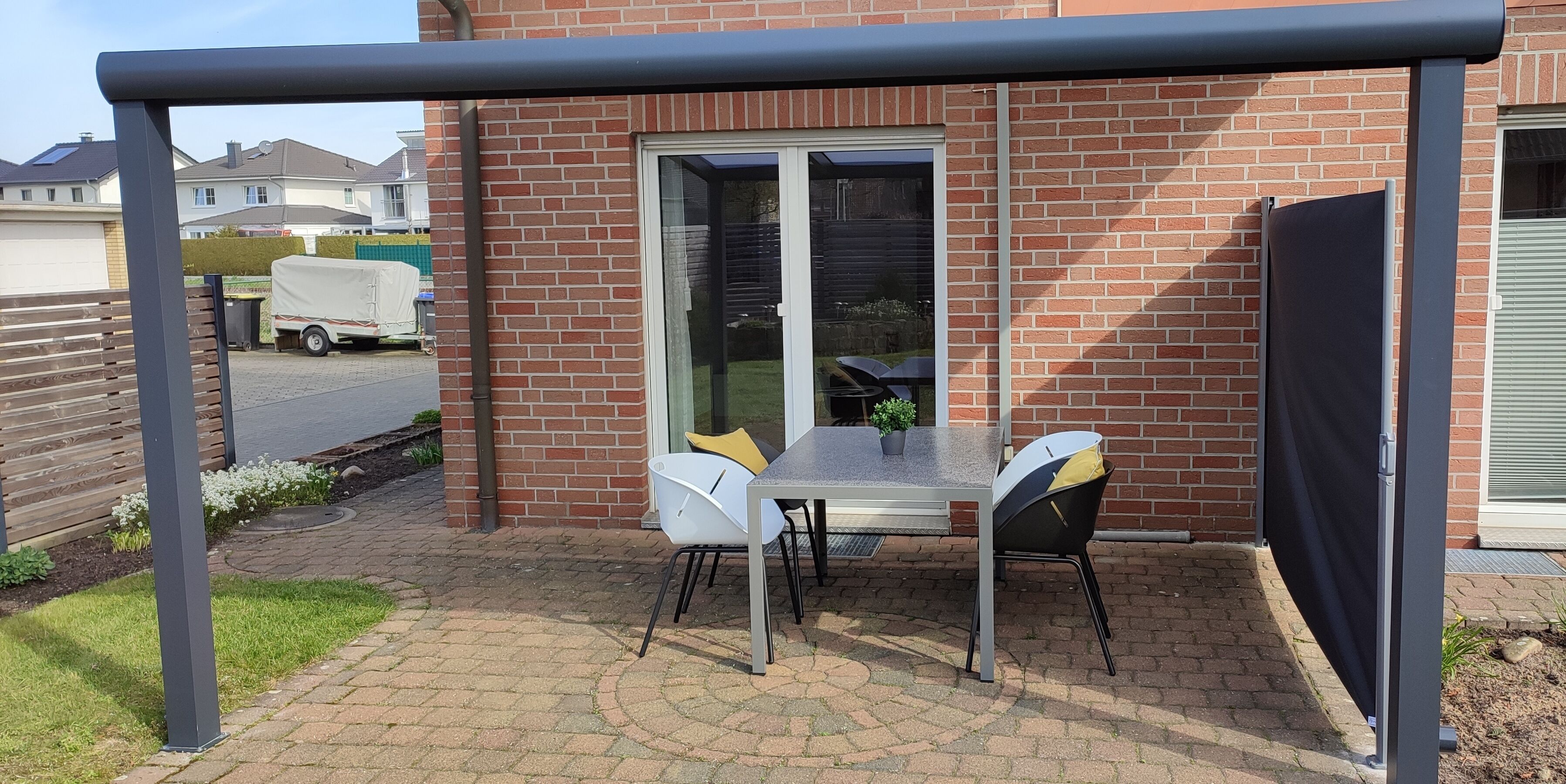 Ein überdachter Patio-Bereich mit Tisch, Stühlen und einem Blumentopf, sowie eine Glastür zum Verschieben.