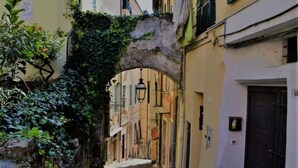 A narrow alleyway with a stone archway covered in greenery, flanked by buildings with balconies and doors. - Cristina Home "Town Center" (Sanremo)