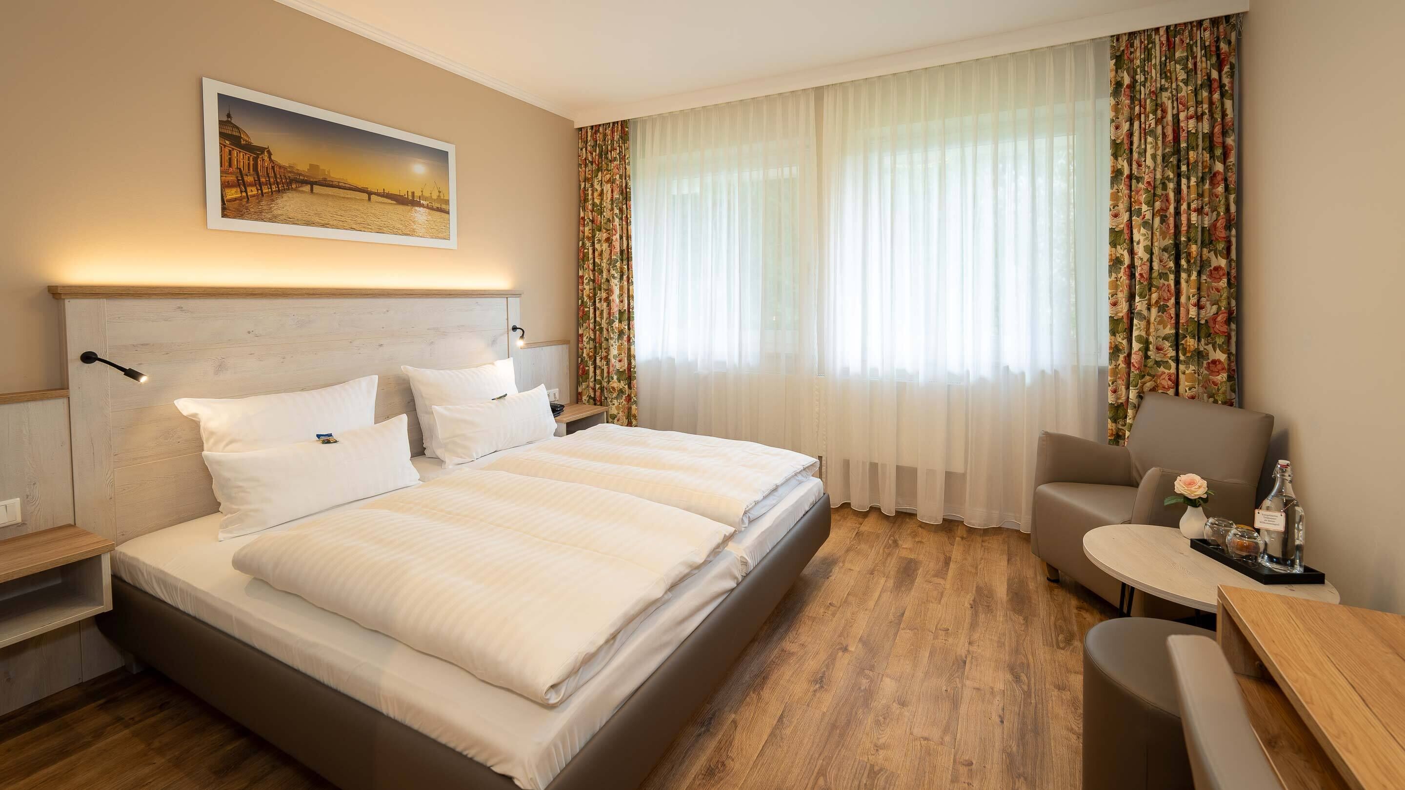 A hotel room with a large bed, a desk, a chair, and a painting on the wall.