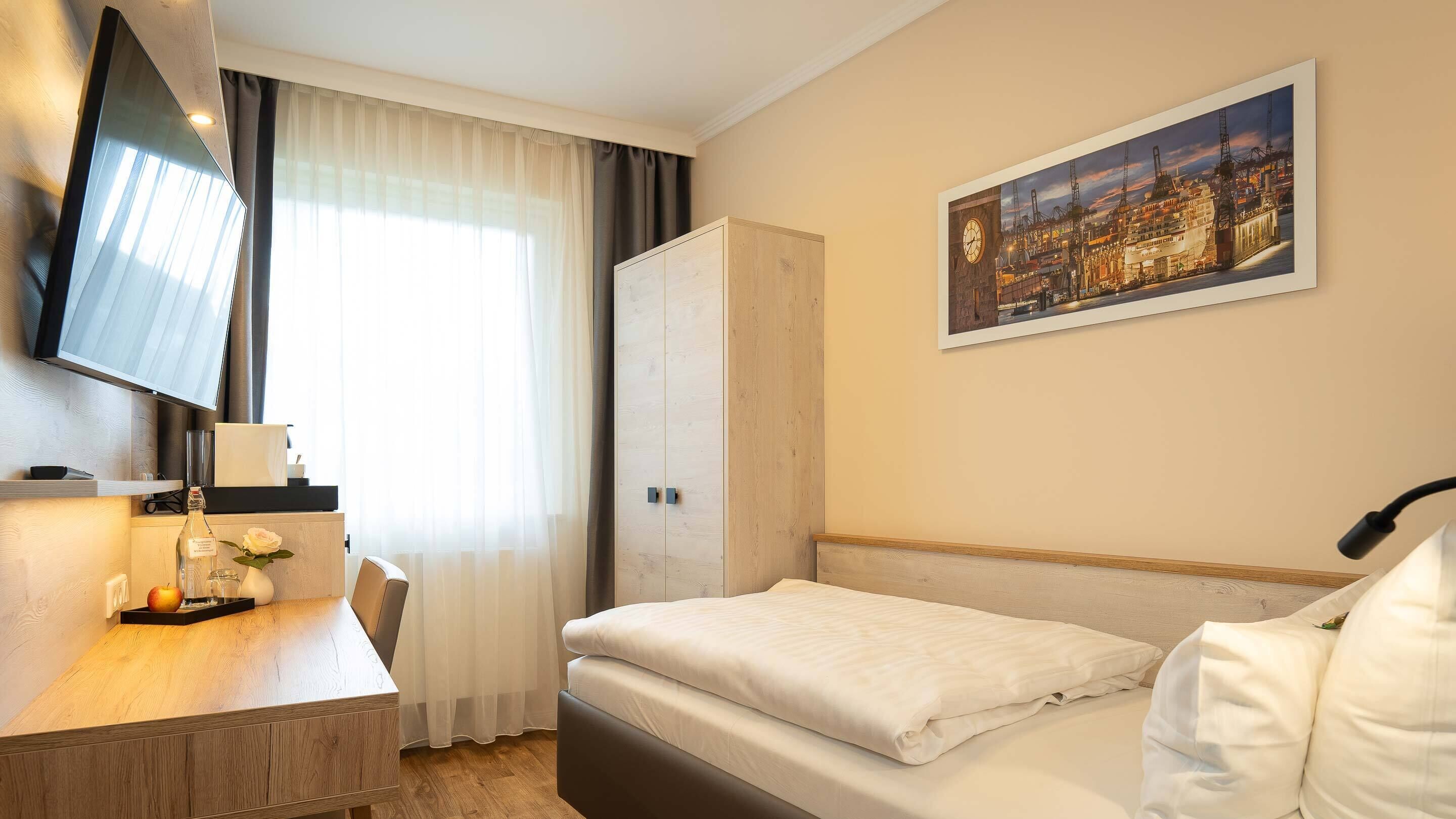 Ein Hotelzimmer mit Bett, Schreibtisch mit Fernseher, Kleiderschrank und Stadtbild an der Wand.