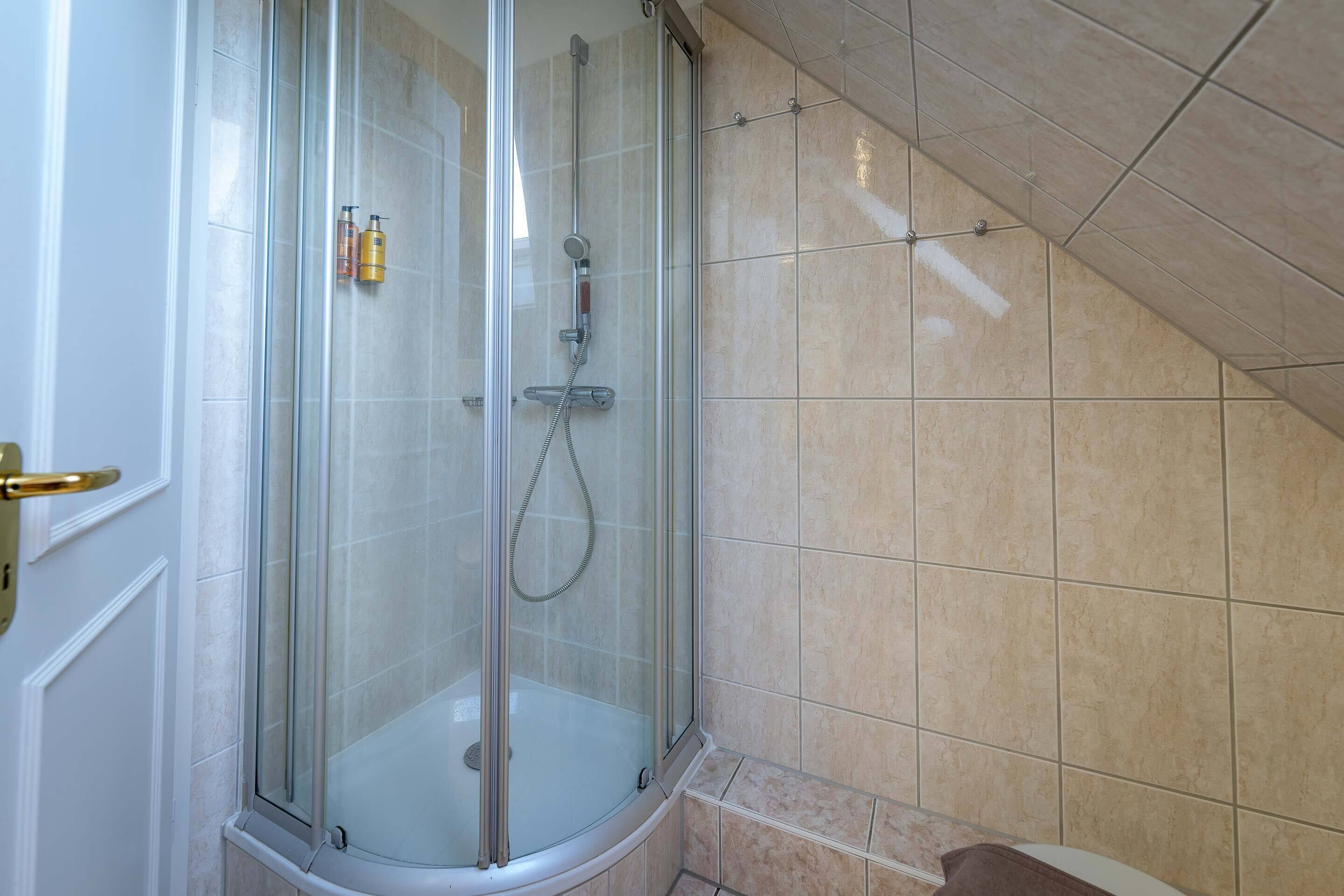 Ducha con cerramiento de vidrio, cabezal de ducha de mano y grifo empotrado.