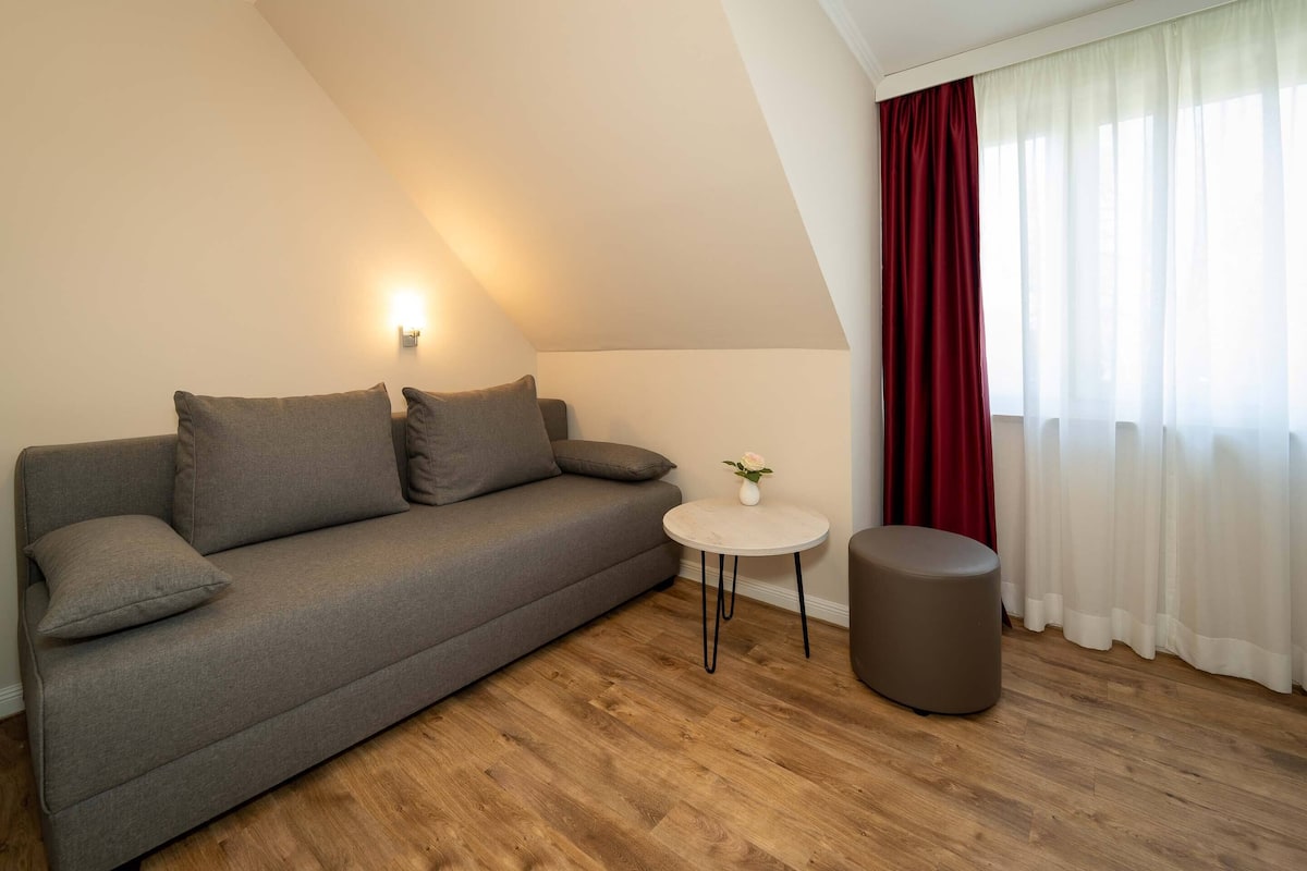 A modern living room with a grey sofa, a small round table with a vase, and a round ottoman.