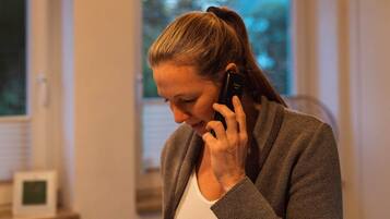 A person standing indoors, holding a mobile phone to their ear.