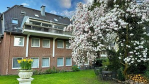 Una casa de ladrillo de dos pisos con jardín, un árbol con flores rosadas y césped.