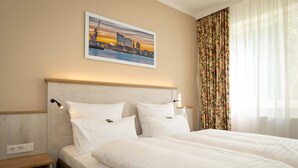 Una habitación de hotel con una cama, una mesita de noche, un cuadro de un paisaje urbano y cortinas florales.