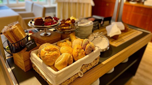 Una mesa de buffet con diversos productos horneados y pastelería, incluyendo pan, muffins y un pastel.