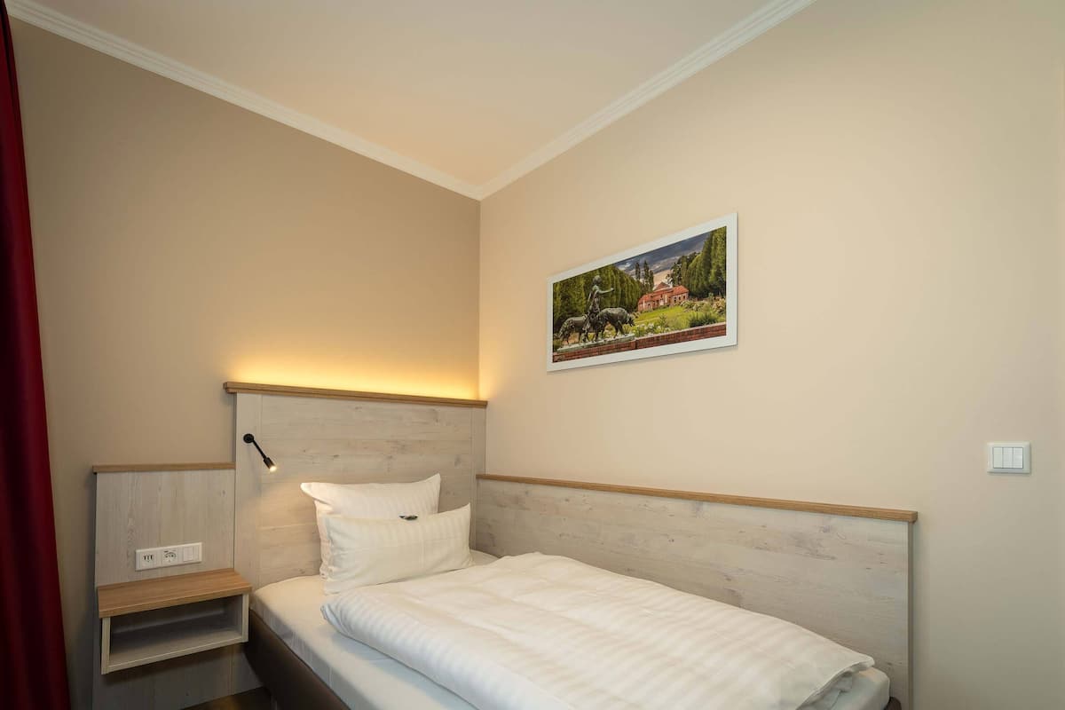 A bedroom with a bed, bedside table, lamp, and a painting on the wall.