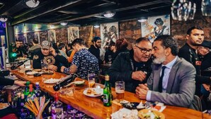 Um bar movimentado com mesas de madeira, garrafas e copos.