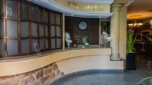 Um saguão de hotel com balcão de recepção, um relógio e uma placa com a inscrição 'HOTEL LAFAYETTE'.
