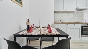 A modern kitchen with white cabinets, a black countertop, and a dining area with a black table set for four. - Sunny Apartment | Balcony and Private Parking (Wrocław)