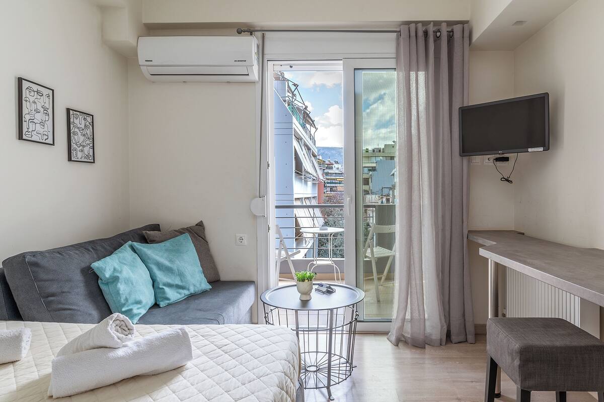 A modern hotel room with a balcony, a sofa, a small table with a plant, and a TV mounted on the wall.