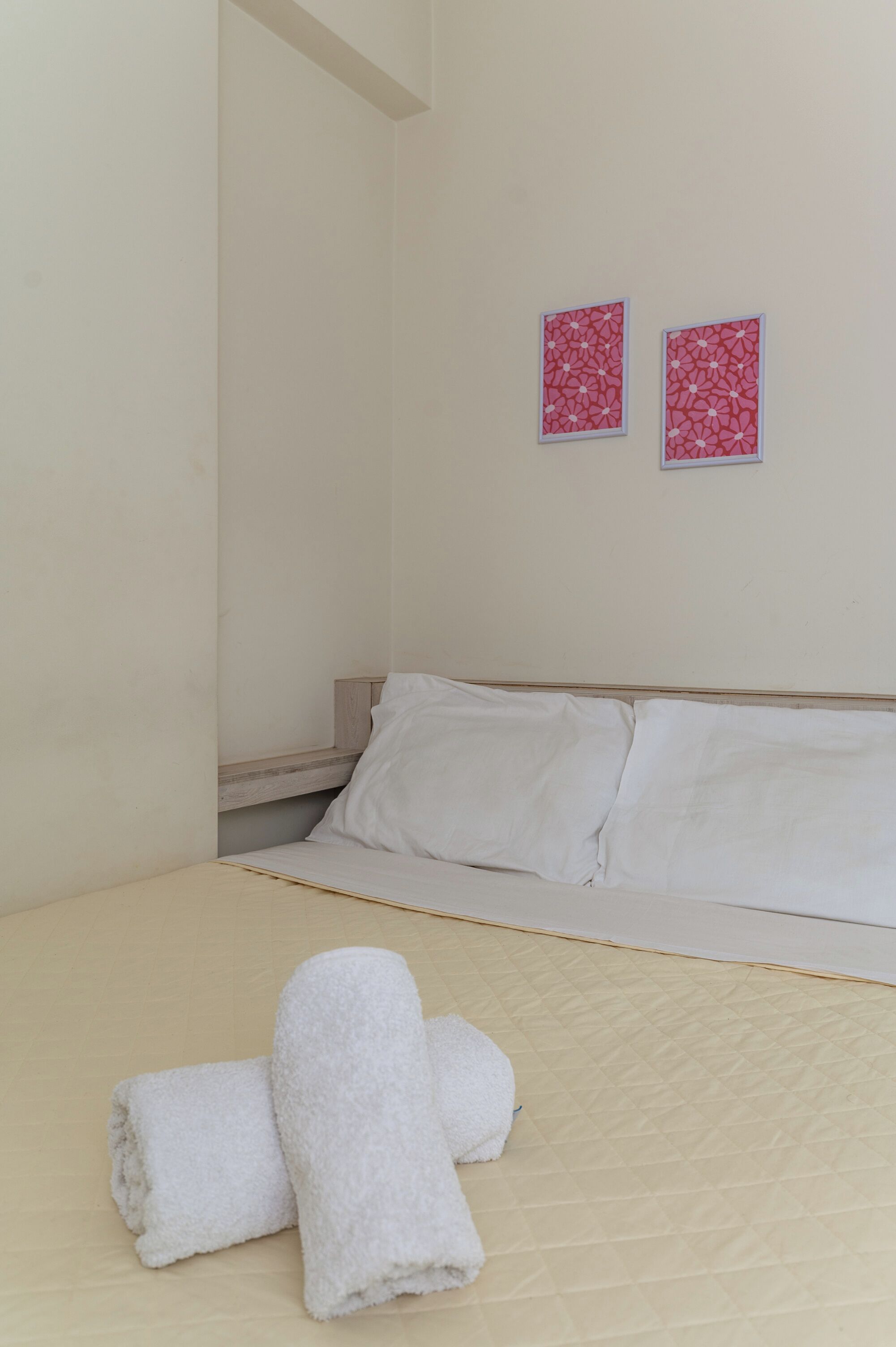 A bedroom with a bed, two pillows, a wooden nightstand, and two wall-mounted pictures.