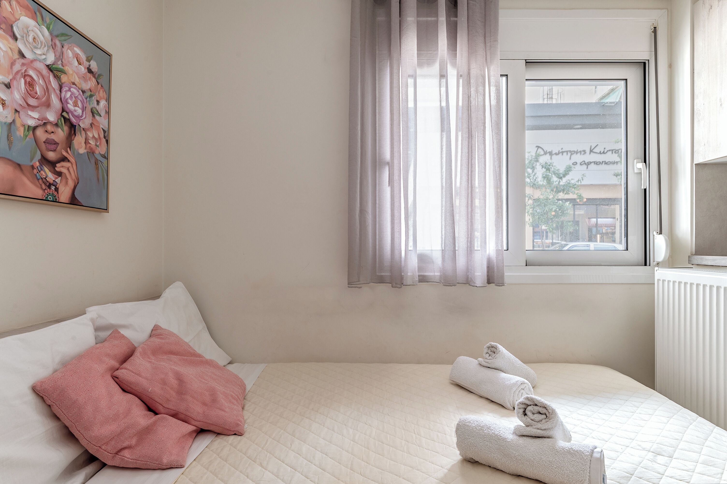 A hotel room with a bed, pillows, a window with curtains, and a painting on the wall.