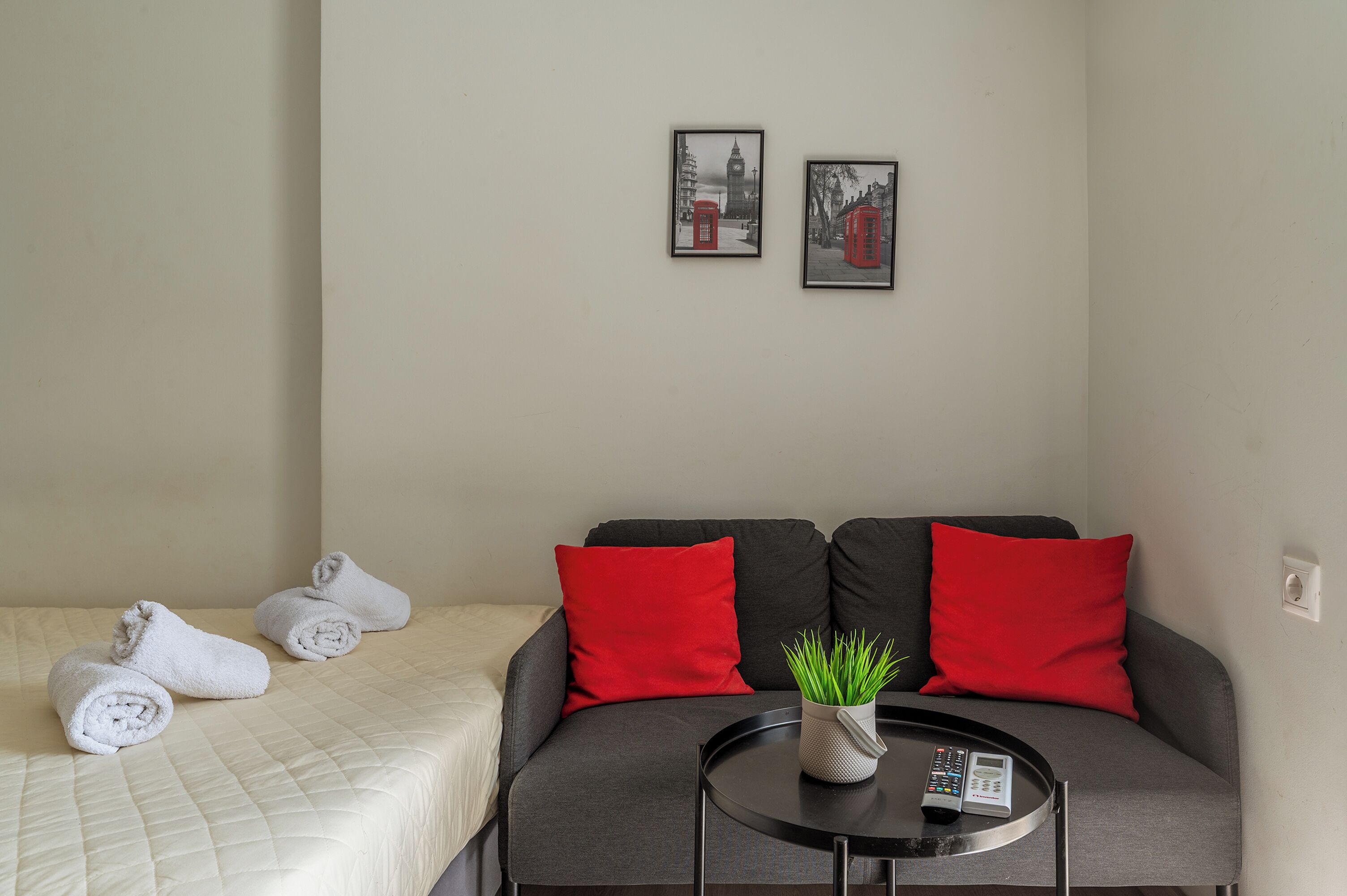 Een hotelkamer met een bed, een bank, een kleine tafel met een afstandsbediening en twee ingelijste foto's aan de muur.