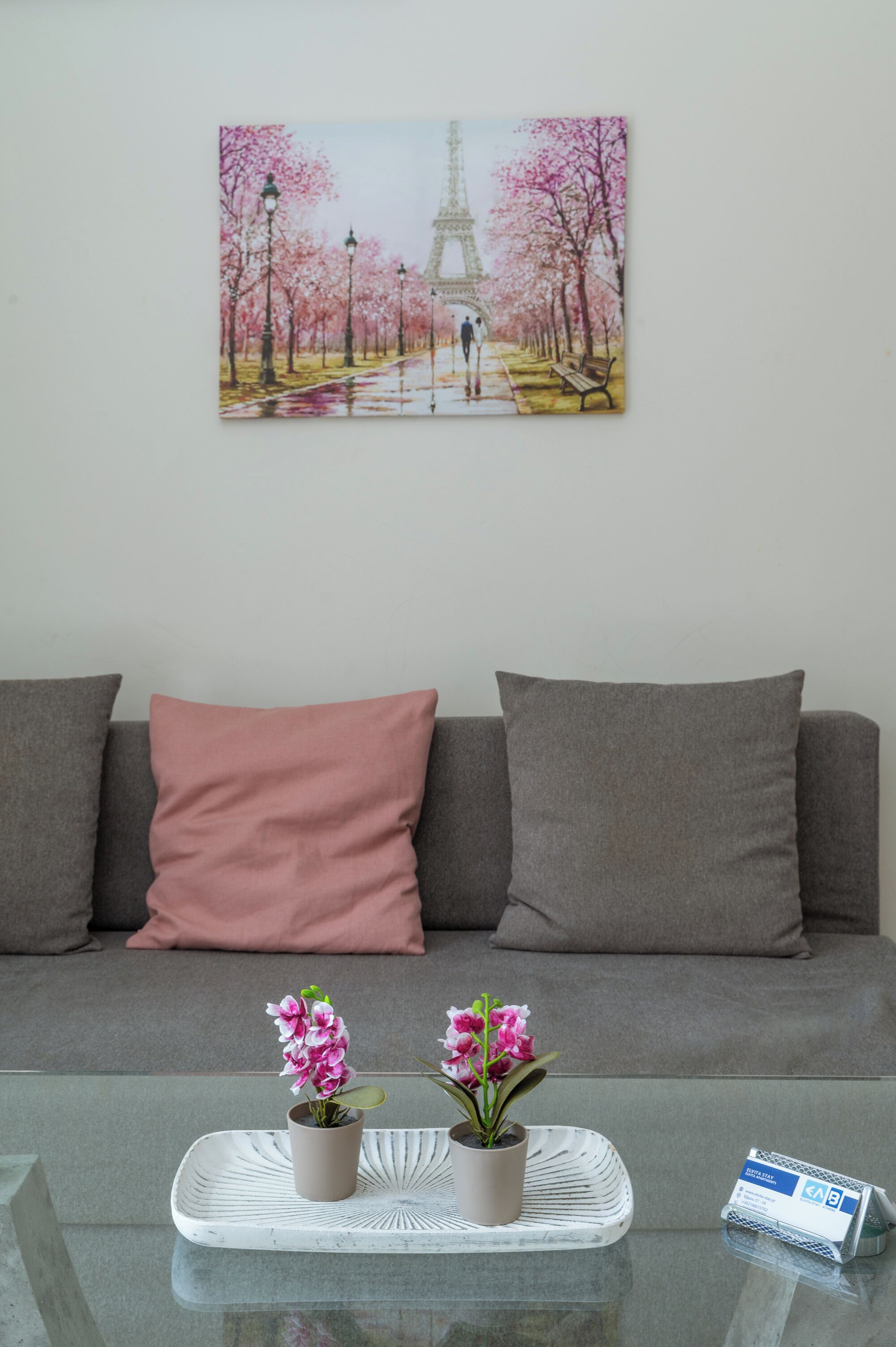 Un salon avec un canapé, une table basse ornée de deux plantes en pot et un tableau encadré représentant la Tour Eiffel.