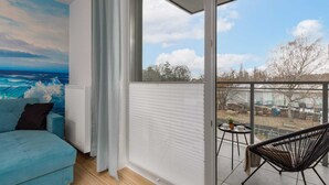 Ein Zimmer mit großem Fenster, einem blauen Sofa, einem schwarzen Sessel und einem kleinen Tisch mit Pflanze.