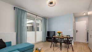 Ein modernes Wohnzimmer mit einer Couch, einem Esstisch mit Stühlen, einem Fernseher und einem Fenster mit Vorhängen.