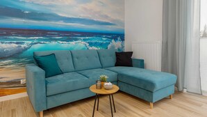 Ein blaugrünes Sofa mit einem kleinen runden Tisch und einem Topf mit Pflanze, vor einer großen Wandmalerei mit Meerblick.