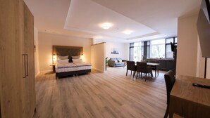 A modern bedroom with a large bed, a dining area with chairs, and a kitchen in the background. - 24 7 Selfcheckin Pferdemarkt (Leer)