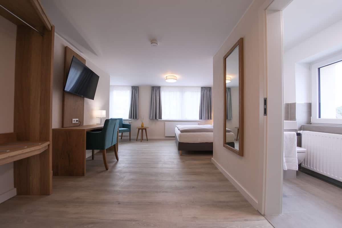 A modern hotel room with a wooden desk, a bed, a TV mounted on the wall, and a large mirror.