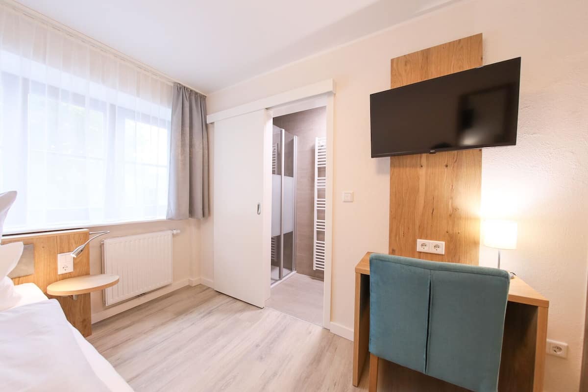 A hotel room with a bed, a bedside table, a TV mounted on the wall, and a view of the hallway.