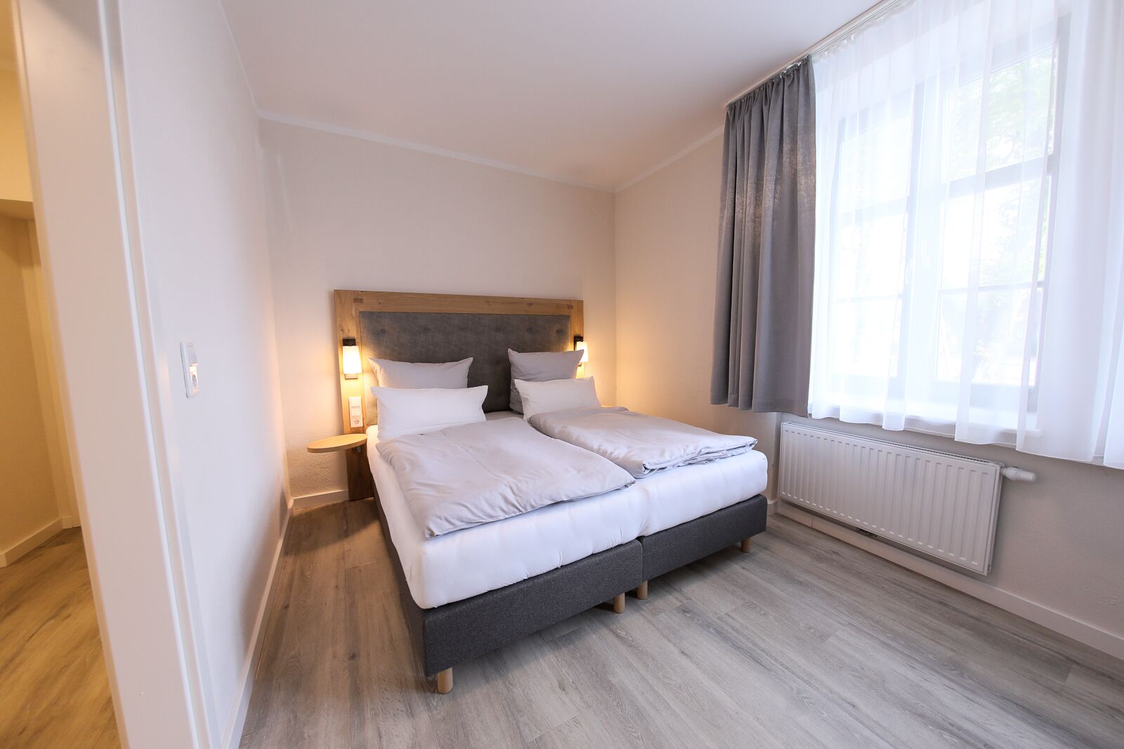 A neatly arranged bedroom with a bed, bedside tables, a window with curtains, and a radiator.