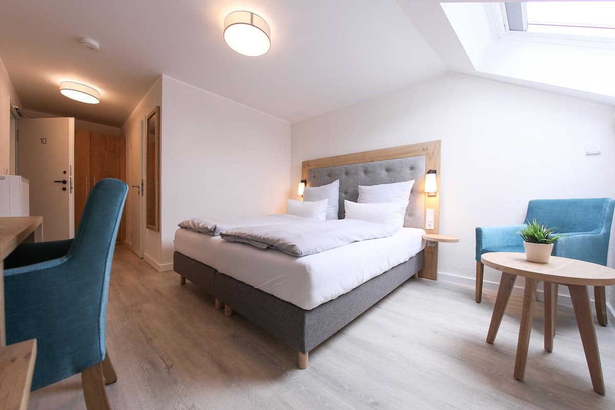 A modern bedroom with a large bed, a desk, a chair, and a small table with a plant.