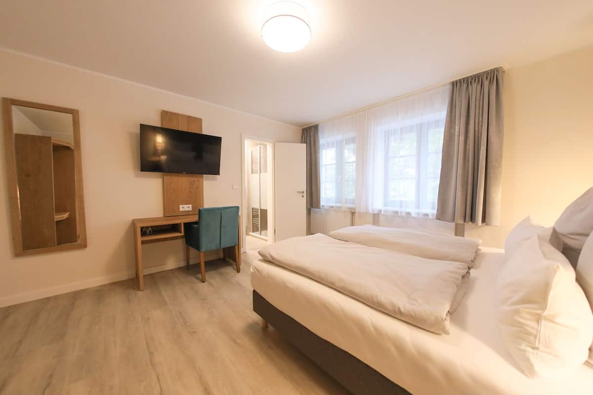 A hotel room with a bed, a desk, a television, and a window with curtains.