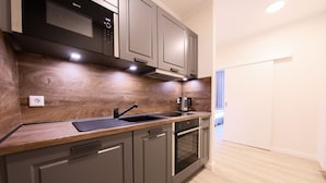 A modern kitchen with grey cabinets, a wooden countertop, a built-in oven, and a coffee maker. - 24 7 Selfcheckin Pferdemarkt (Leer)