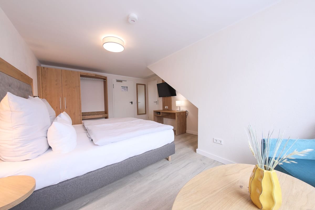 A modern hotel room with a bed, a desk, and a small table with a vase.