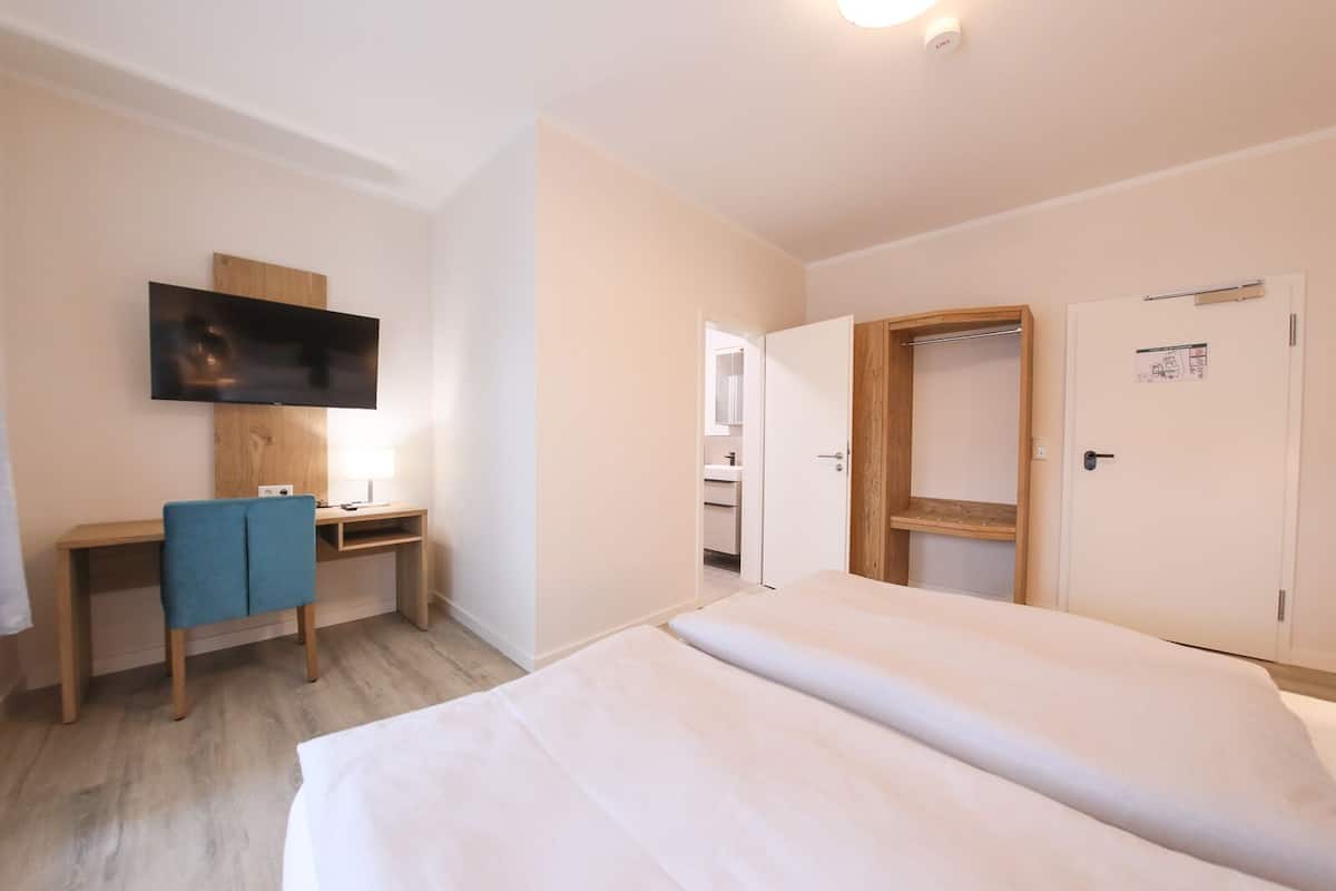 A hotel room with a bed, a desk with a chair, a television, and a wardrobe.
