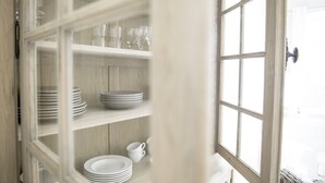 A view through a window into a room with a wooden cabinet containing stacked plates and glasses. - Berliner Hof, Apartment 6 (55sqm), Westerland, Sylt. (Sylt)