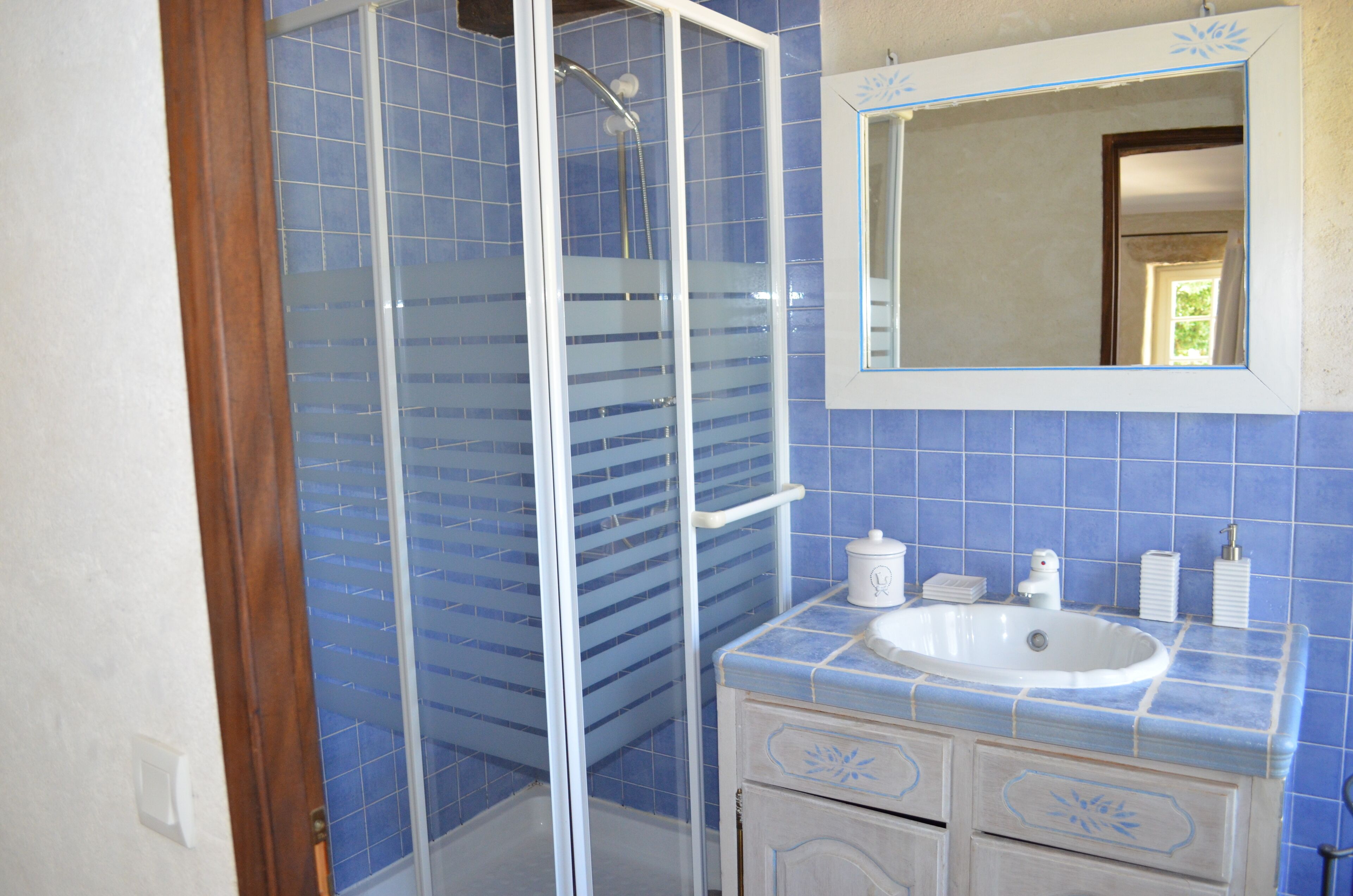 A bathroom with a glass-enclosed shower, a white sink, and blue-tiled walls.