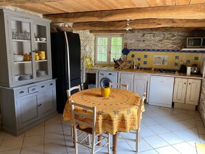 Een landelijke keuken met een eettafel, stoelen, een koelkast, een wasmachine en een magnetron.