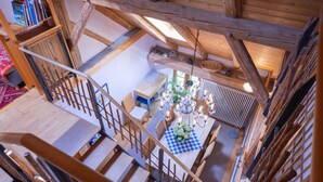 Un escalier en bois mène à un espace repas agrémenté d’une nappe à carreaux, d’un lustre et offrant une vue sur la salle à manger située en contrebas.