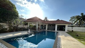 A swimming pool with a tiled deck, a covered seating area, and a house in the background. - Spacious Private Pool Villa (Tambon Rawai)