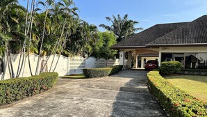 A residential house with a paved driveway leading to a garage, surrounded by well-maintained hedges and palm trees. - Spacious Private Pool Villa (Tambon Rawai)