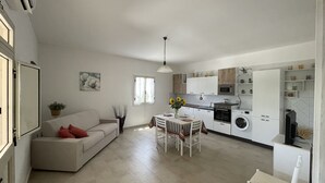 Eine moderne Küche mit weißen Schränken, einem Esstisch mit Stühlen, einer Couch und einem Fernseher.