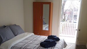 Quarto com cama, guarda-roupa e porta para uma varanda.
