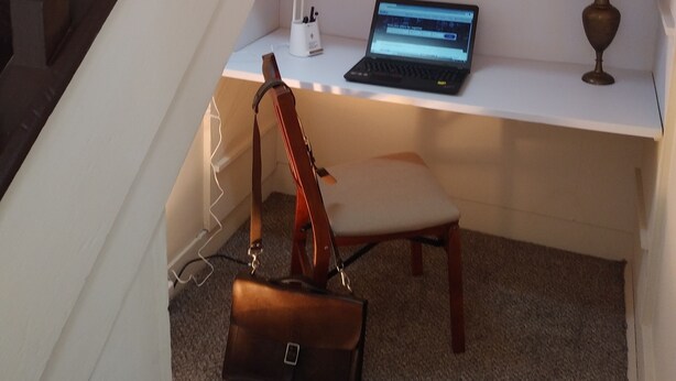 Um espaço de escritório em casa com um laptop, uma luminária de mesa e uma cadeira.