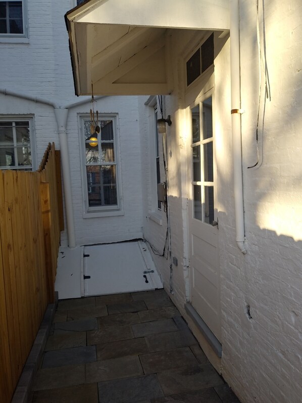 A narrow stone-paved courtyard with a wooden fence, white walls, and a window with a hanging light fixture. - Sunlight 2BR townhouse w/ private parking in Downtown Frederick (Frederick)