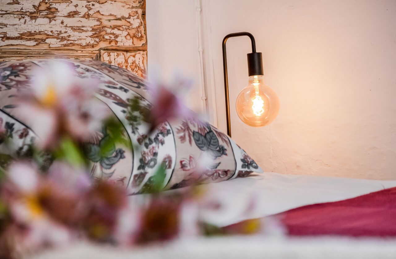Ein Bett mit einem blumigen Kissen und einer Wandleuchte.